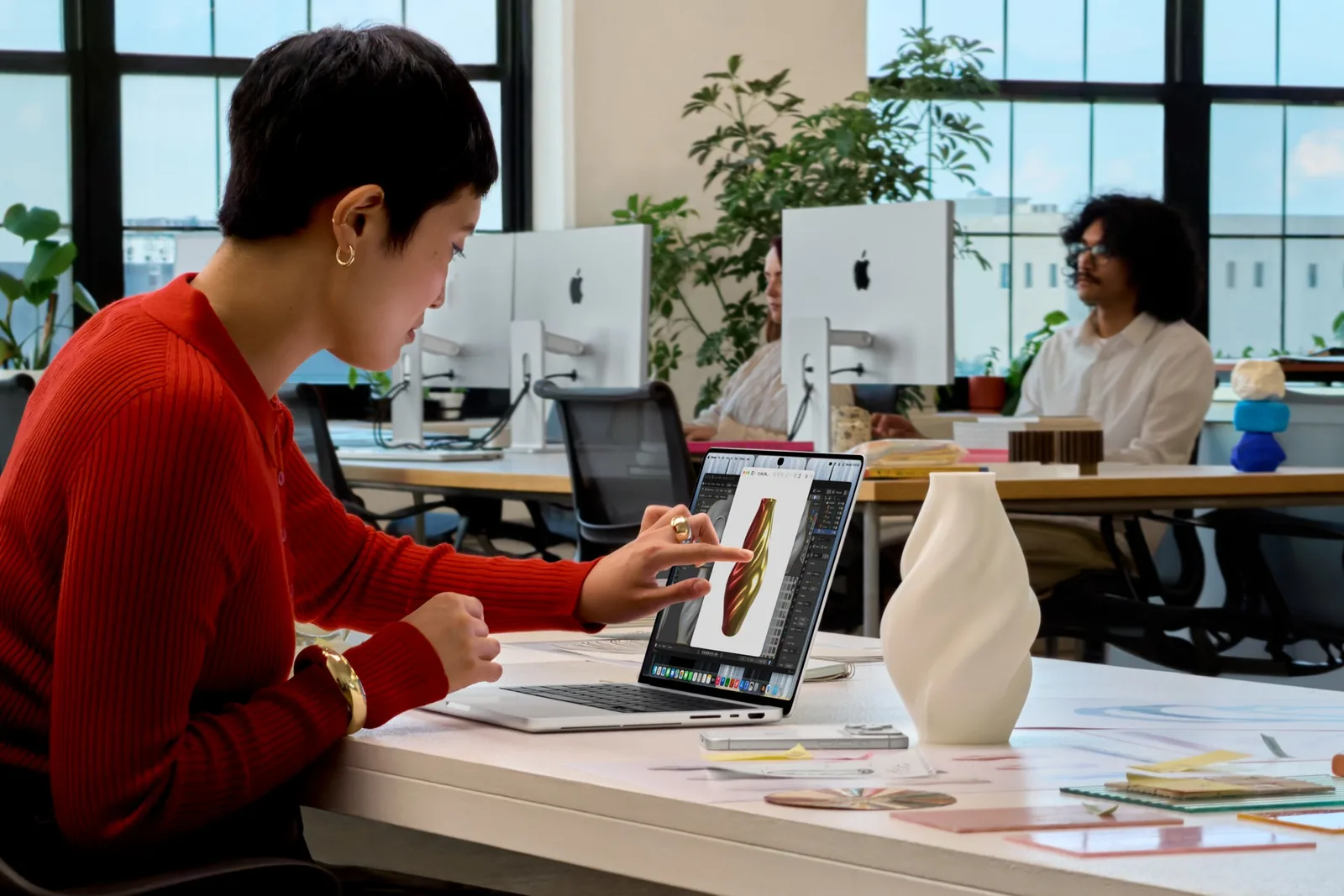 A person at an office desk reaches up and touches the screen of a MacBook Pro with PROLED XDR Display.